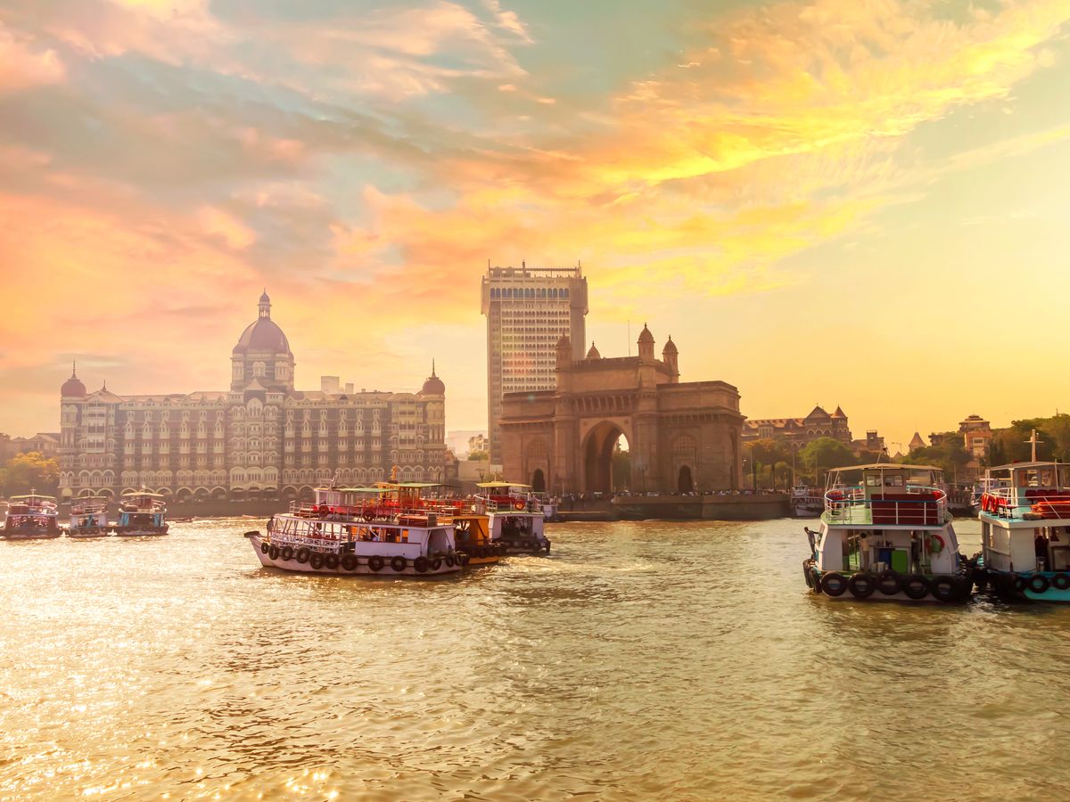 The Gateway of India and boats in Mumbai Harbour under a warm sunset sky